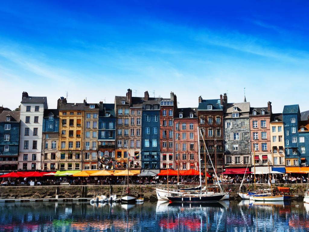 Waterfront of Honfleur harbor in Normandy, France against a blue sky.