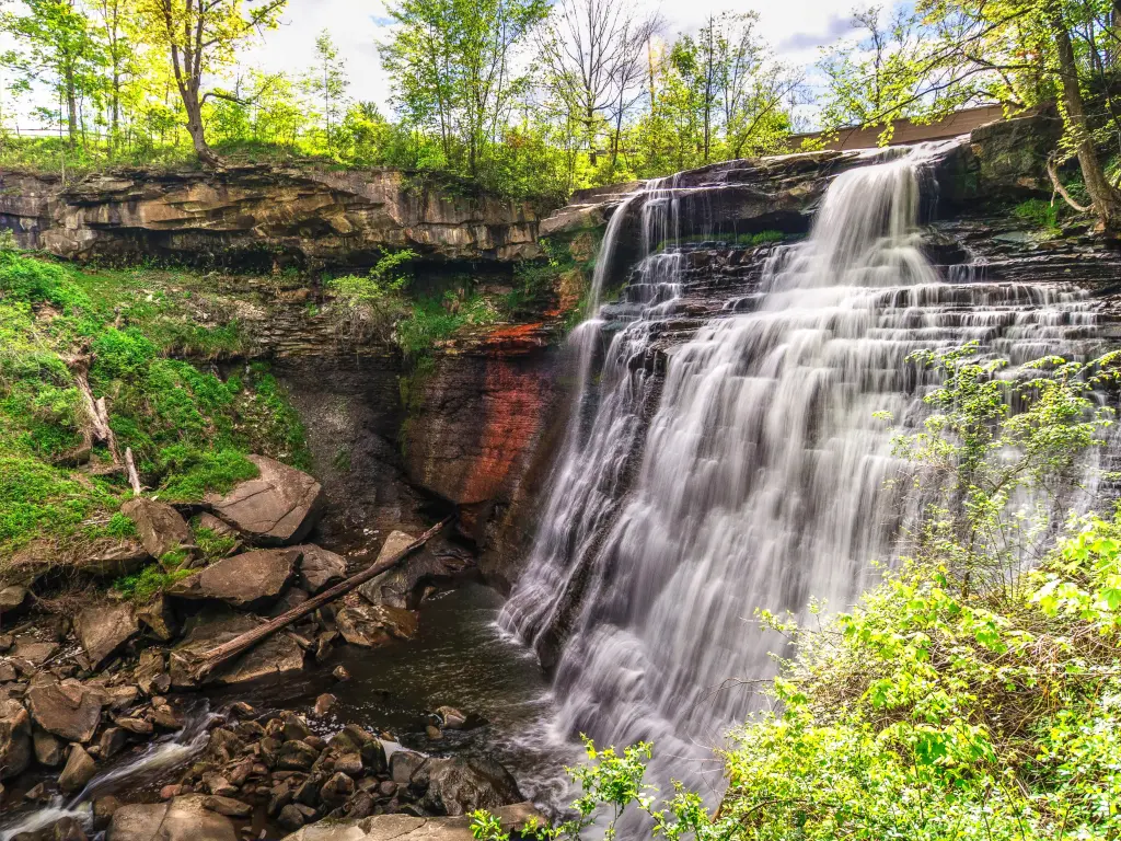 Cascading water spills into the basin below at Brandywine Falls. The mammoth waterfall is set amidst dense foliage and river rock at Cuyahoga Valley National Park in Ohio
