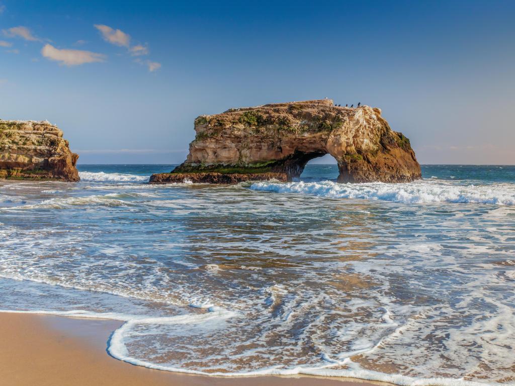Santa Cruz, California, USA with the arches at Natural Bridges State Beach taken on a sunny day with a sandy beach in the foreground.