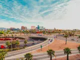 A scenic view of the cars driving along the intersecting highway with palm trees and bushes planted along the road with a picture of the skyscrapers of Phoenix in a fine day with a thin sheet of clouds covering the blue sky