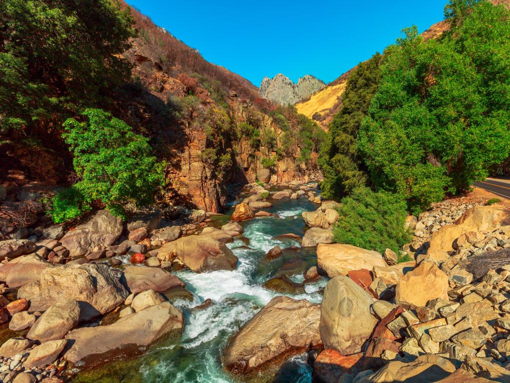 White water river flows through rocky channel with orange coloured rocks and road running alongside