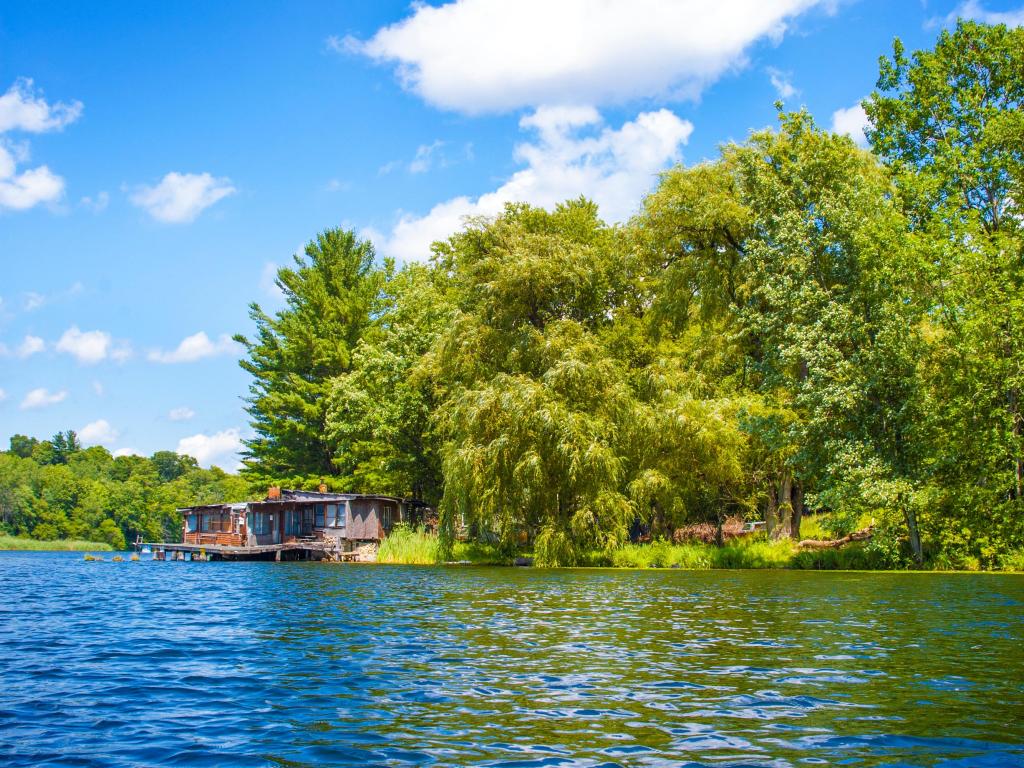Blue sky, calm waters and greenery along the shoreline at Saratoga Lake, with small kayak shack in the background