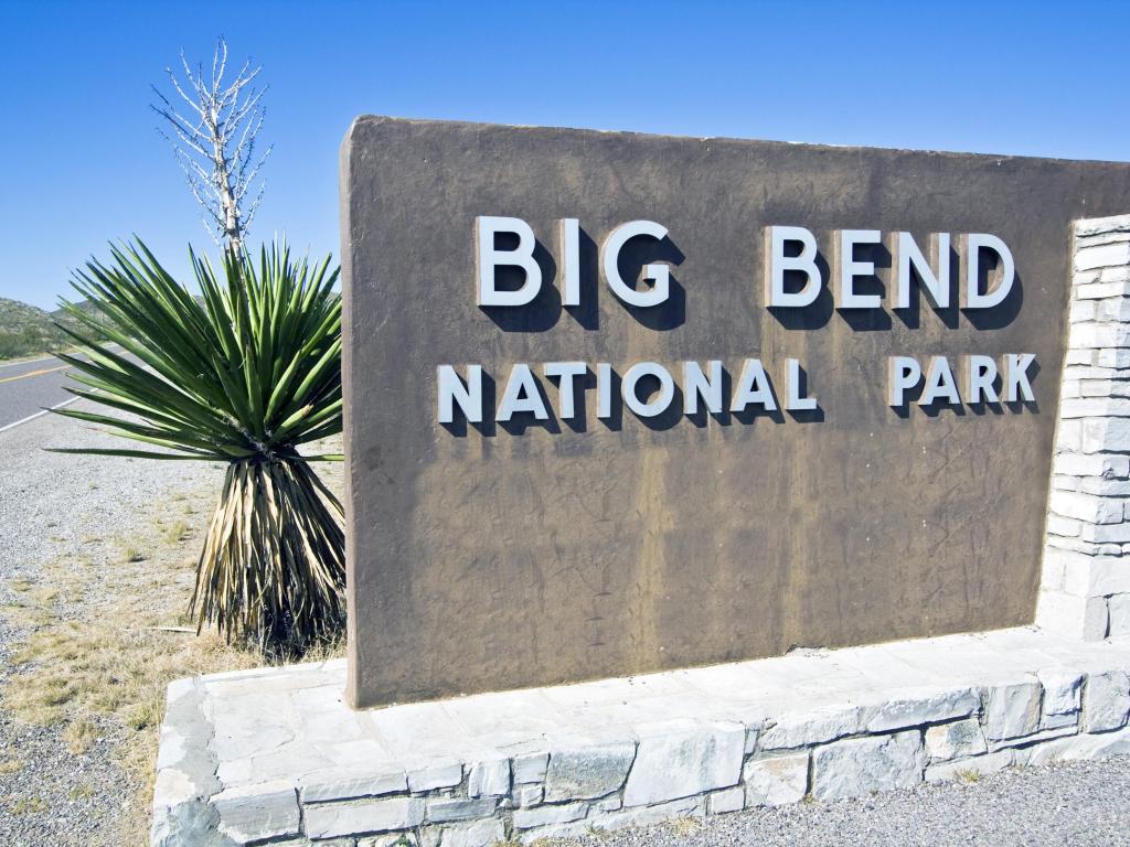Close up of Big Bend National Park Welcome Sign, with palms and open road in the background