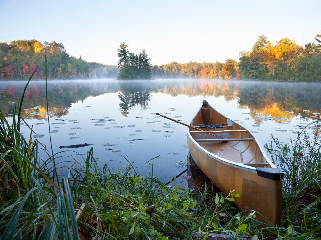 Brainerd lakes, Minnesota, USA with a yellow canoe on shore of calm lake with island at sunrise during autumn.