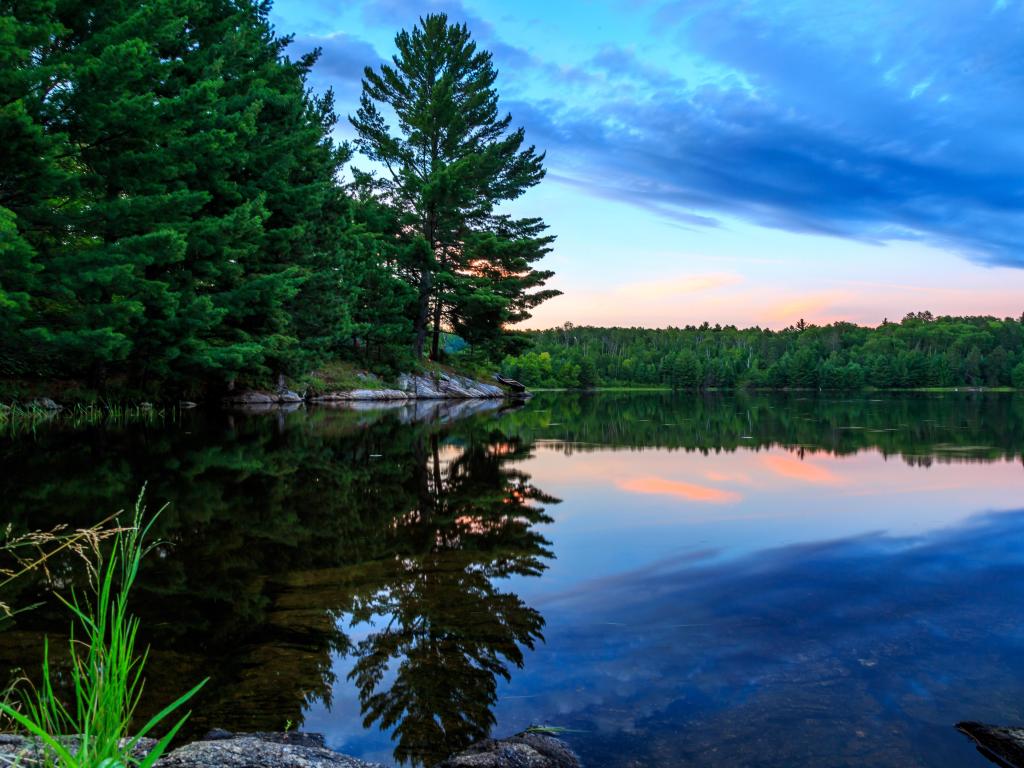 Voyageurs National Park, US/Canada border at sunset with calm waters surrounded by rocks and trees in the distance. 