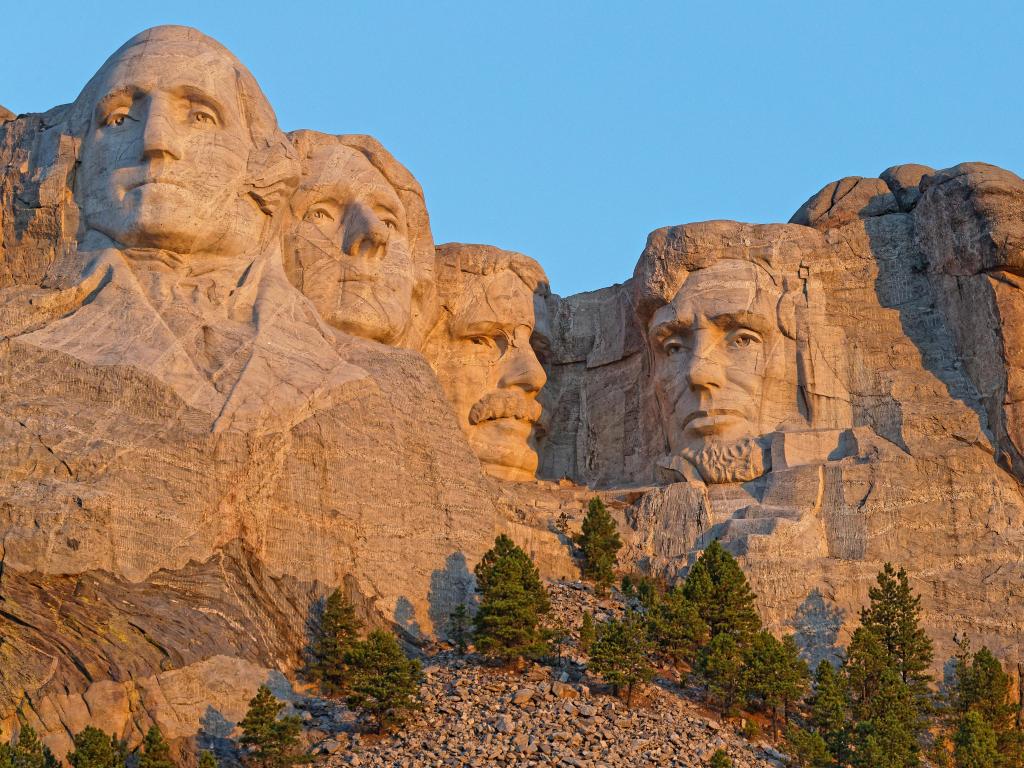 Mount Rushmore, South Dakota, USA with the sculptures of Four United States Presidents at sunrise against a blue sky.