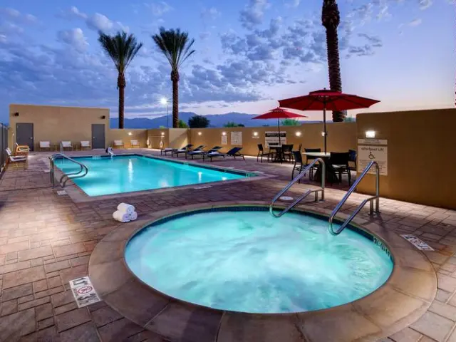 An outdoor pool with loungers surrounding it during sunset with two palm trees in the background