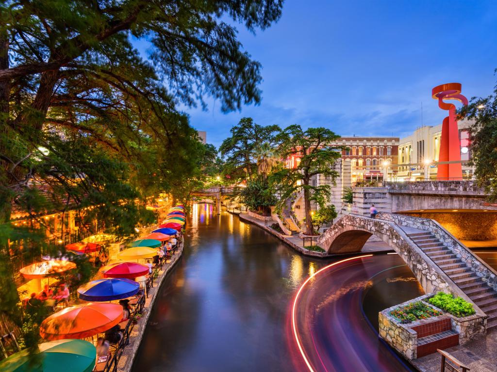 Bright lights and colourful umbrellas along the sides of a calm river through the city at night