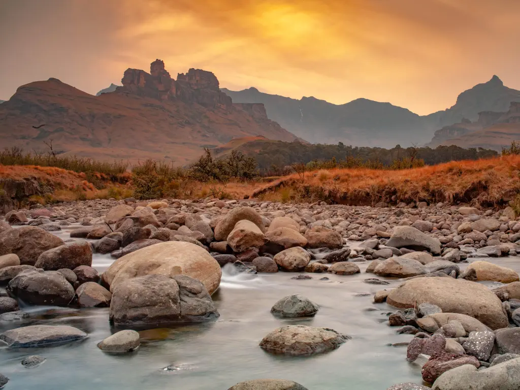 Majestic mountain range in the distance with a stream in the foreground during an orange sunset