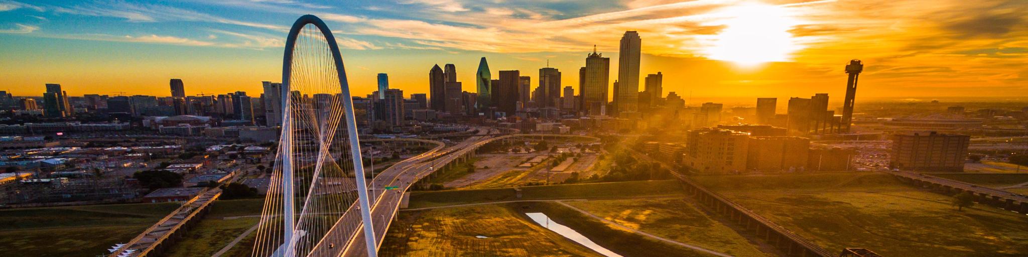 Drone view of the city's skyline with a suspension bridge connecting through over Trinity River Park during sunrise