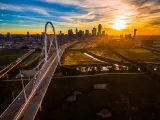 Drone view of the city's skyline with a suspension bridge connecting through over Trinity River Park during sunrise