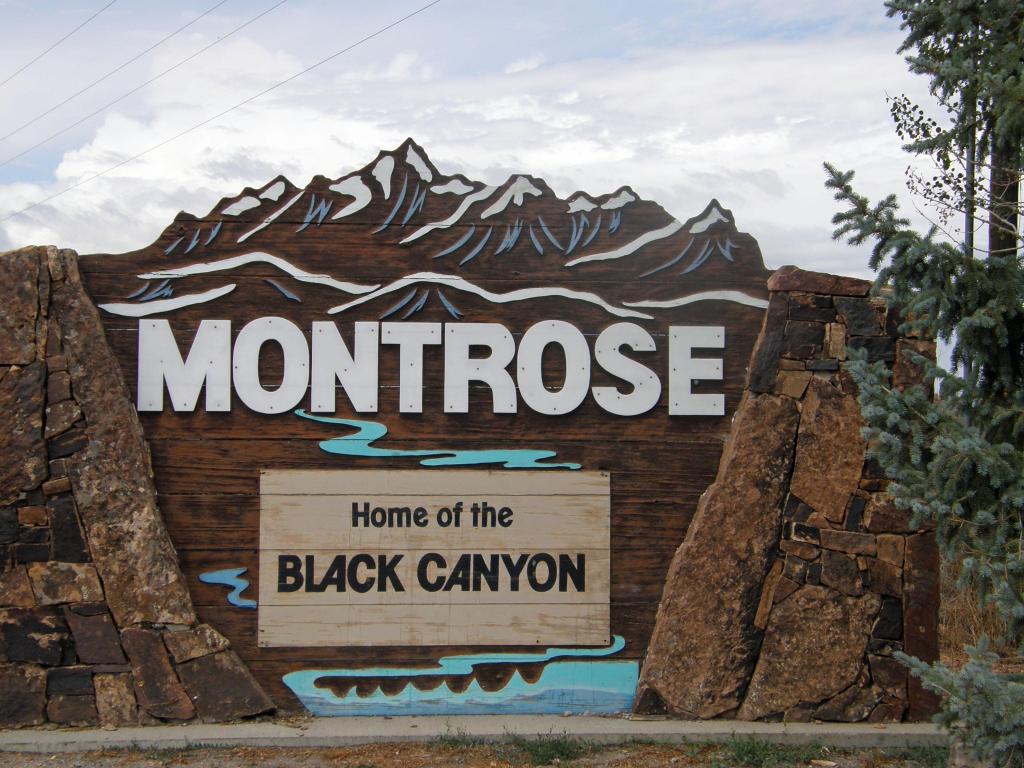 A large wooden sign welcoming visitors to the city of Montrose, Colorado. It reads "Montrose. Home of the Black Canyon"