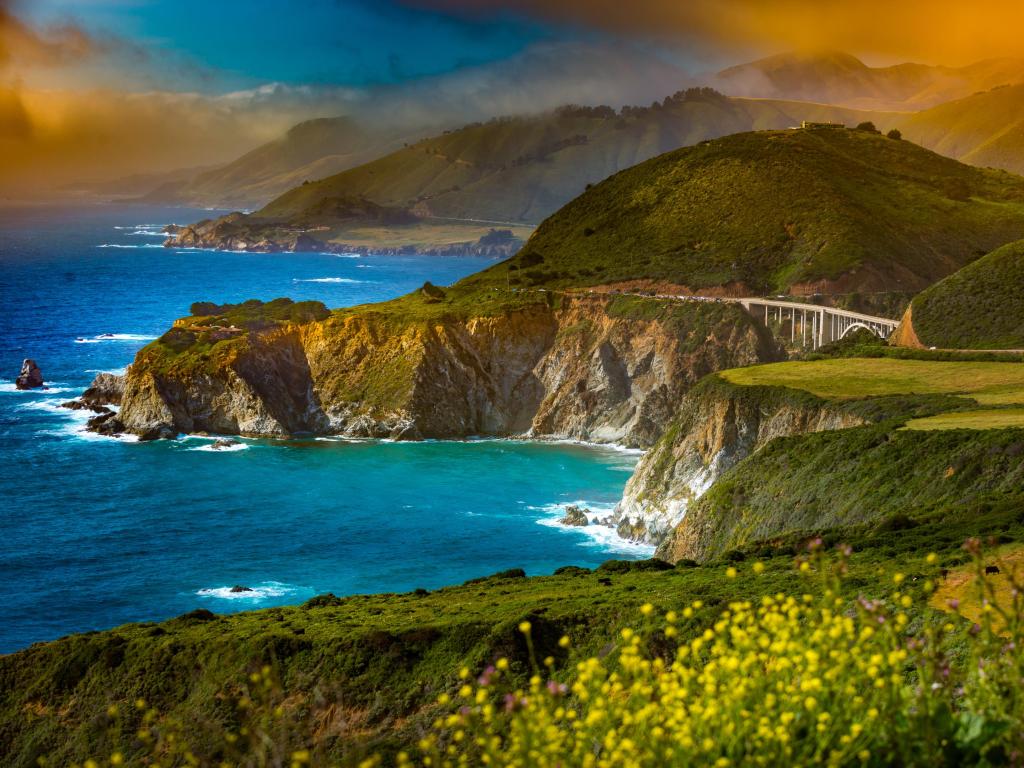 Vibrant blue sea and golden sunlight with Pacific Coast Highway winding along rocky cliffs