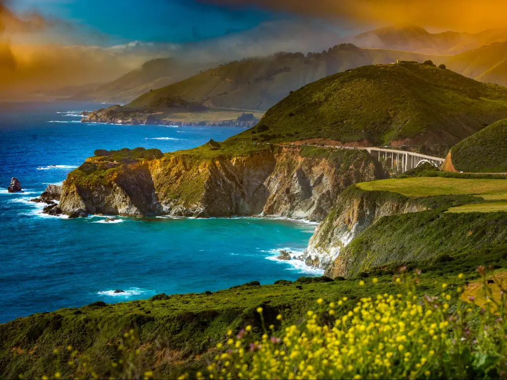 Vibrant blue sea and golden sunlight with Pacific Coast Highway winding along rocky cliffs