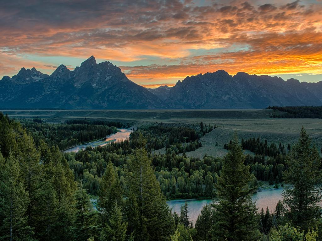 Winding river reflecting pink sunset light with rugged mountains in the background