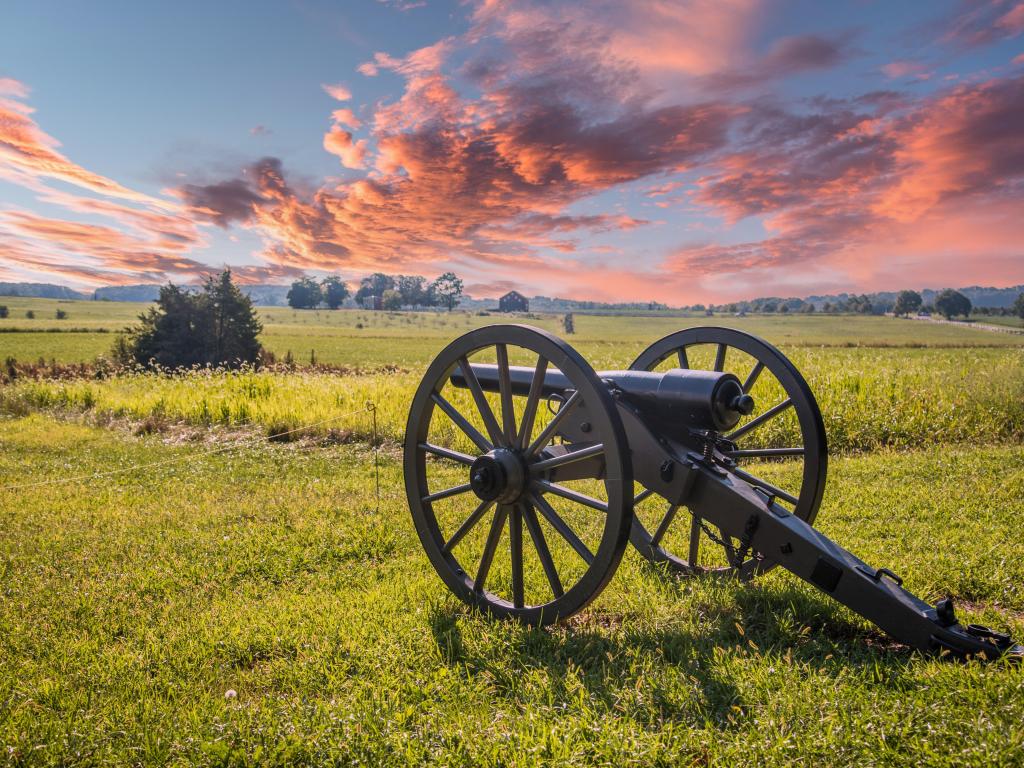 Gettysburg, USA with a canon aiming at a battlefield surrounded by grass and taken at sunset with a beautiful sky above.