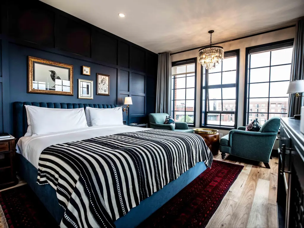 Deluxe suite at The Ramble Hotel, Denver, with dark blue furnishings and panelled walls, and city views from floor to ceiling windows