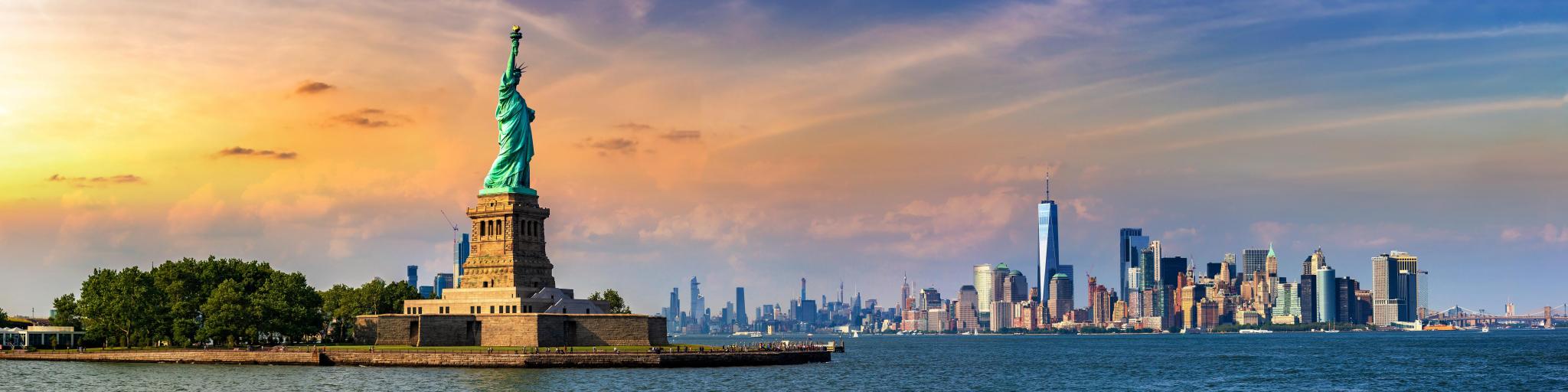 Panoramic view of Manhattan in the distance with the Statue of Liberty in view during sunset