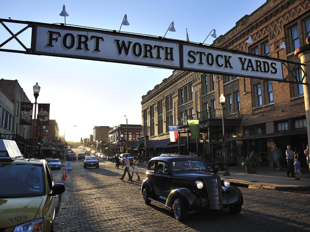 Vintage car drives along brick paved street with historic buildings