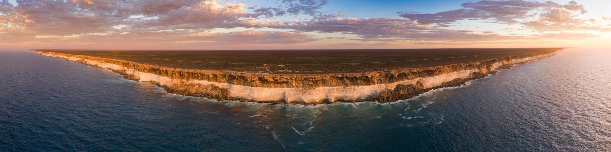 Nullarbor, South Australia taken as an aerial shot of Bunda Cliffs in the distance and the sea in the foreground as the sun is setting.