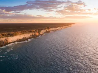 Nullarbor, South Australia taken as an aerial shot of Bunda Cliffs in the distance and the sea in the foreground as the sun is setting.