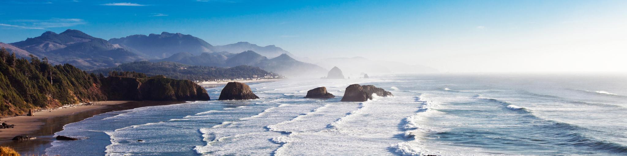 White foam waves lapping along Cannon Beach shoreline with Haystack Rock in the background