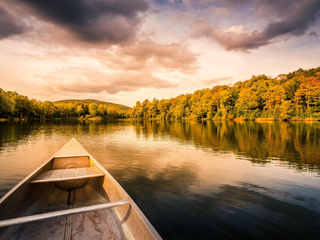 Aluminium canoe on a mountain lake with trees lining the banks and a cloudy sky