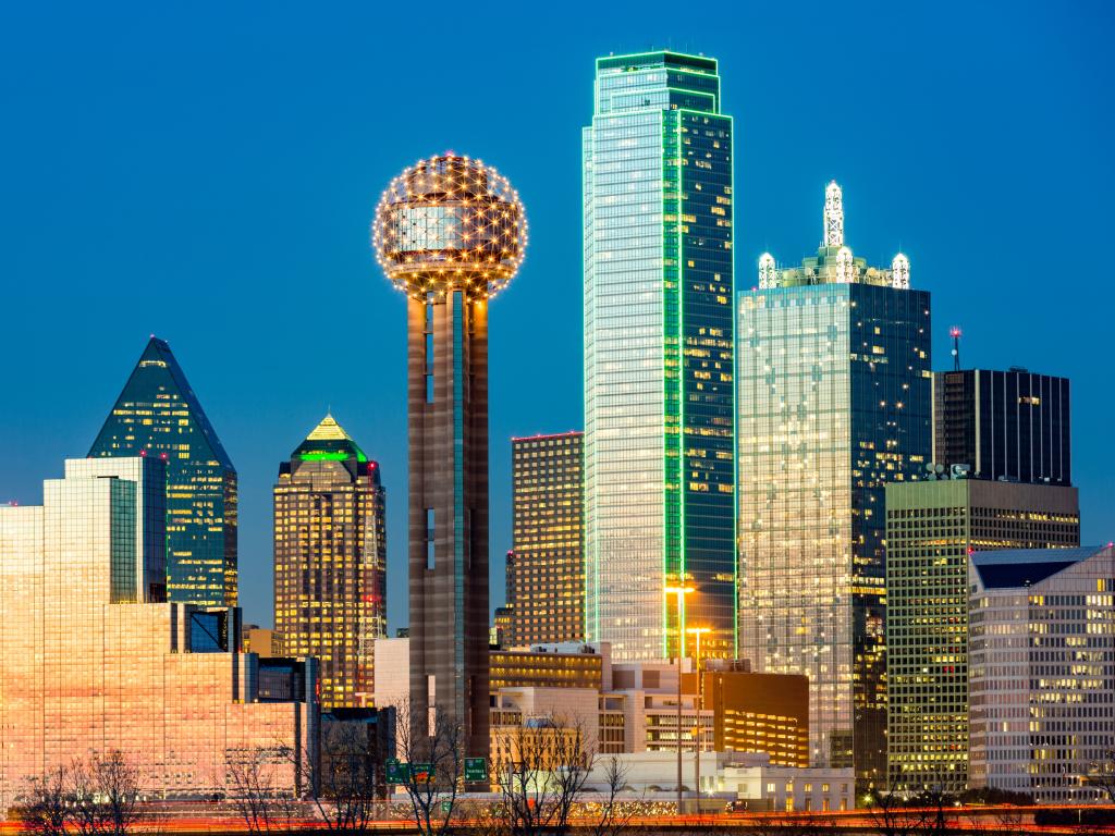 The Reunion Tower in front of the Dallas skyline at night