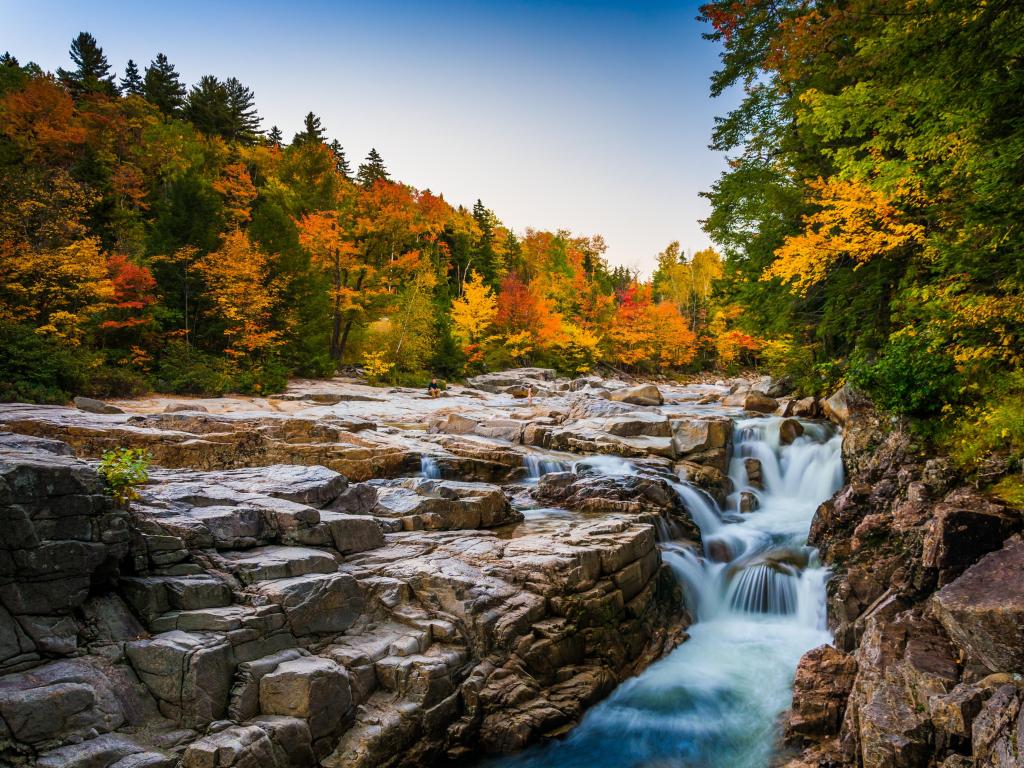 White Mountain National Forest, New Hampshire with autumn colors and waterfall at Rocky Gorge in the foreground, a vast expanse of trees in the background on a clear sunny day.