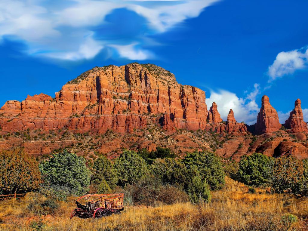 Red cliffs contrasting with bright blue sky with trees and dry grass landscape