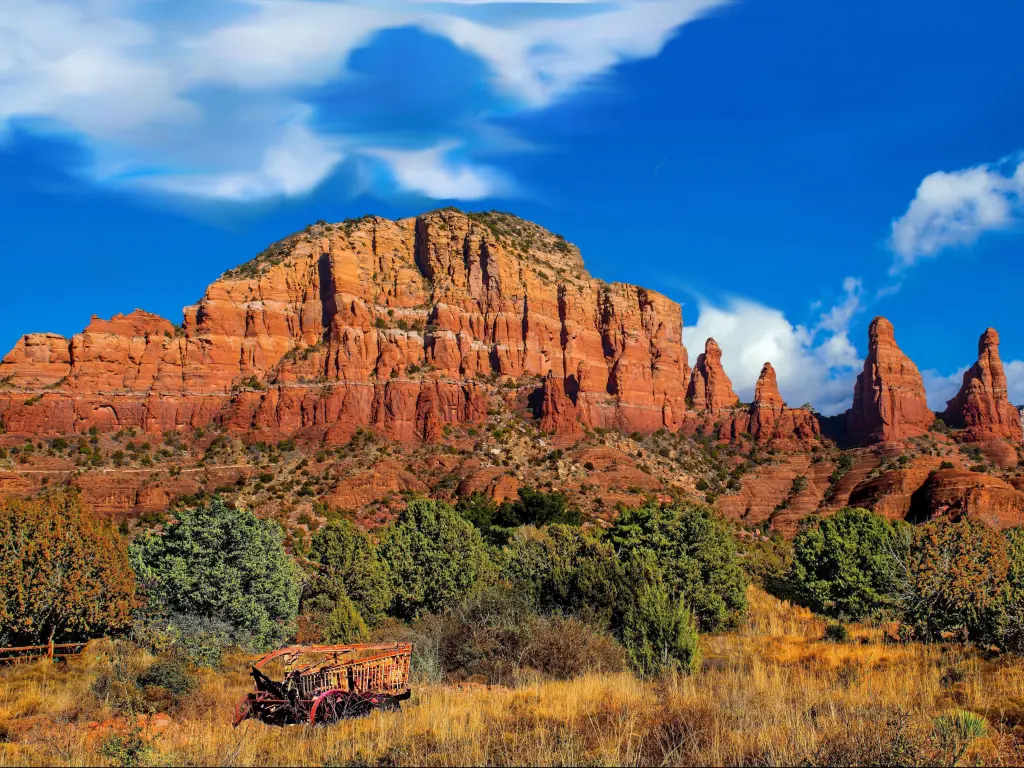 Red cliffs contrasting with bright blue sky with trees and dry grass landscape