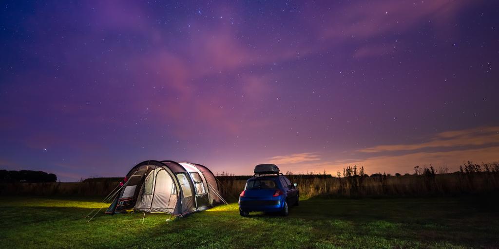 Tent and car under the night sky on a road trip