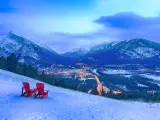 Two red chairs on a hill in the snow, overlooking the city as the night falls