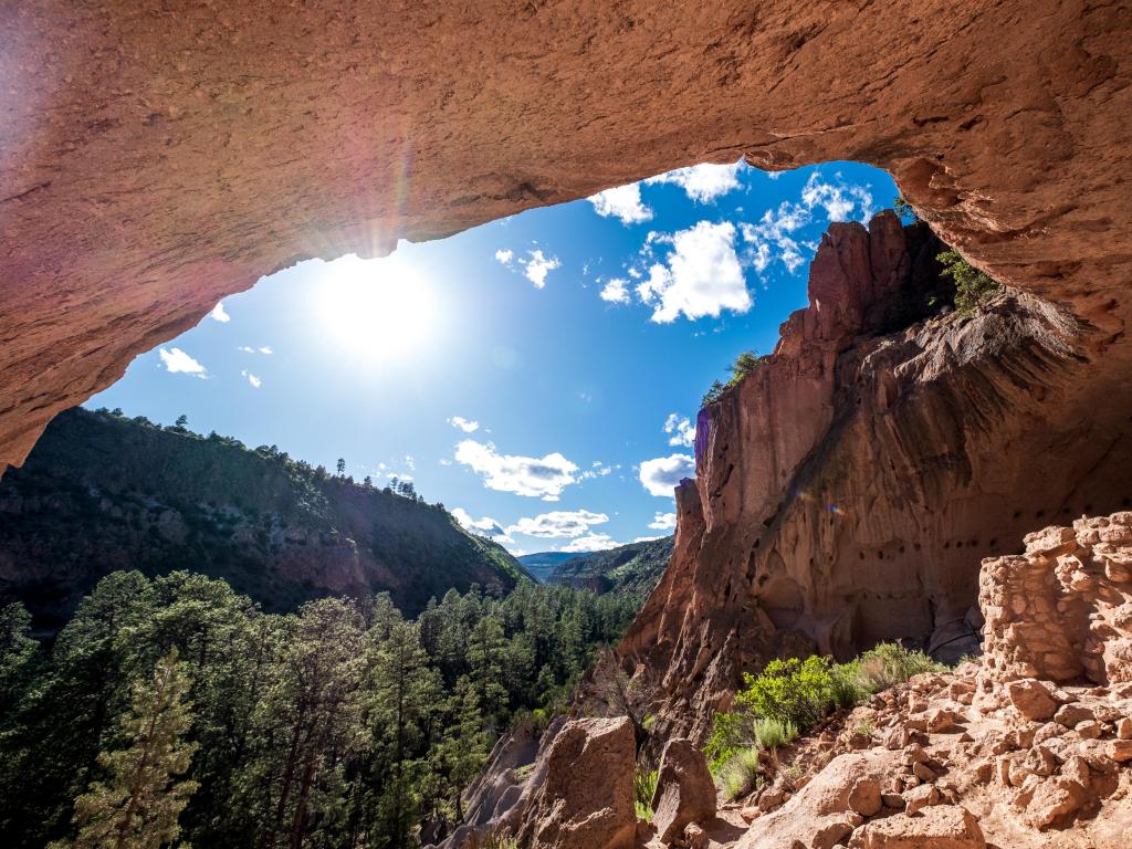 Bandelier National Monument, New Mexico, USA with an alcove in the foreground and framing the trees and rock formations in the distance on a clear sunny day. 