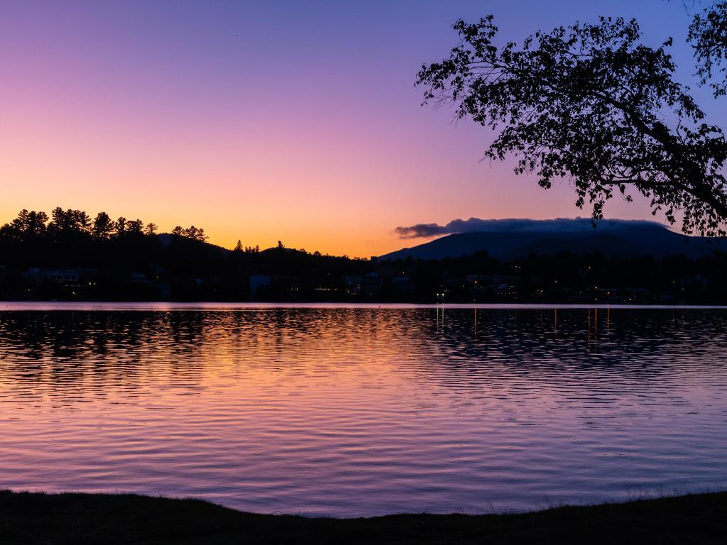 Lake Placid, NY, USA with a beautiful, colorful rainbow sunset over a lake with forest and mountains silhouettes in the background. 