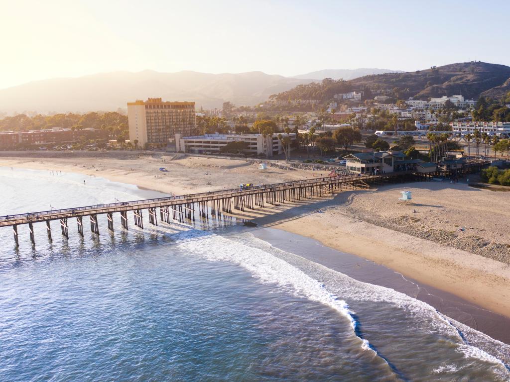 San Buenaventura State Beach, California with an aerial view of downtown Ventura with a pier over the sea, mountains in the background on a hazy sunny day.