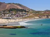 View across the ocean at Avila Beach, with the sandy shores and coastline dotted with sunbathers and swimmers, and pier jutting into the water