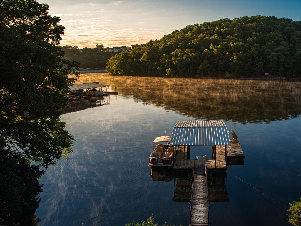 Osage Beach, MO, USA taken at early morning sunlight illuminated wood covered hills across a calm reflecting lake with dock in foreground at Lake of the Ozarks