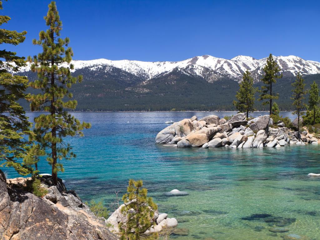 Crystal clear lake with trees and snow-capped mountains in the background