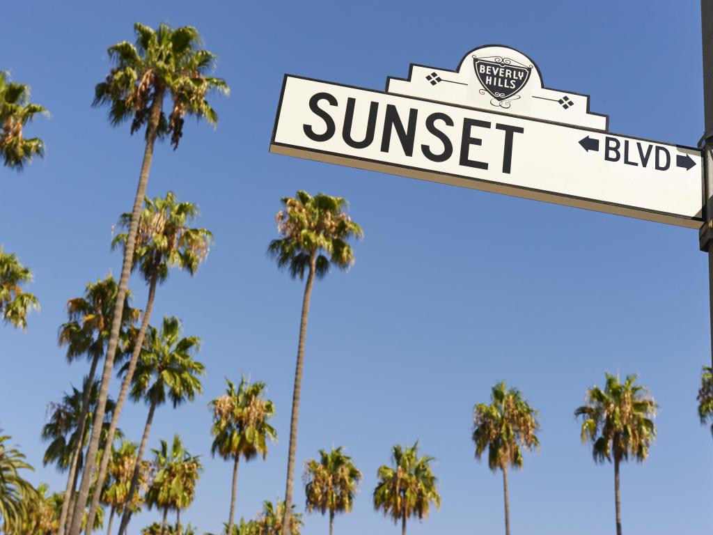 Sign post for Sunset Boulevard, Beverly Hills in Los Angeles, California, with palm trees in the background, set against a blue sky