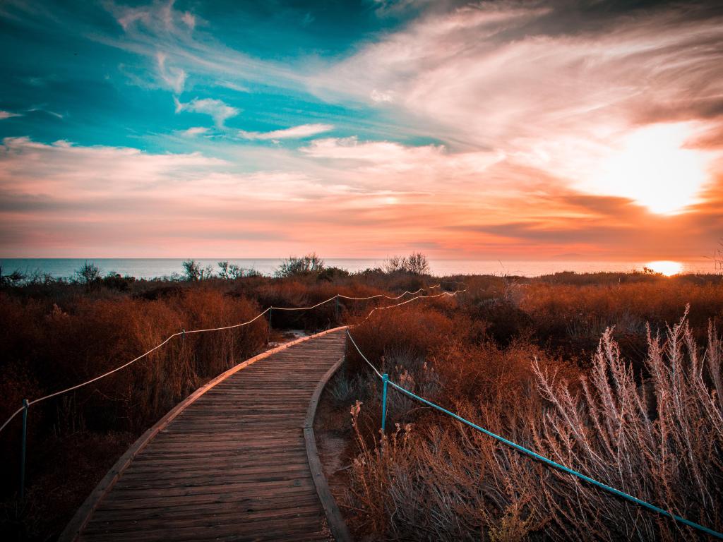 Crystal Cove State Park, California, USA with a boardwalk leading to grassy dunes and a sun set in the distance.