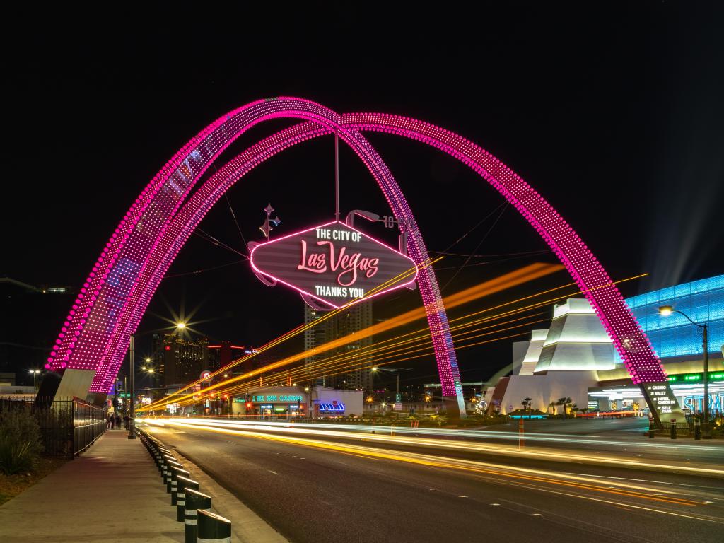 Neon-lit Las Vegas Boulevard Gateway Arch at night with a sign that reads 