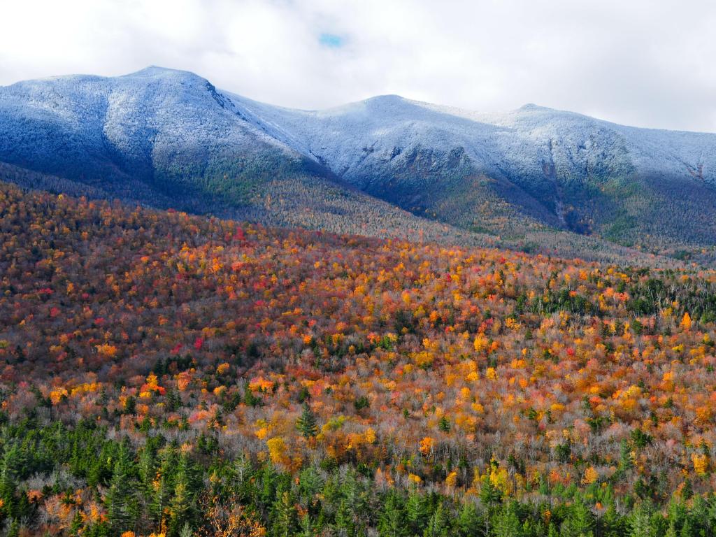The White Mountains, New Hampshire, USA taken during the fall with yellows and oranges in the foliage in the foreground and low cloud above the mountains in the distance.