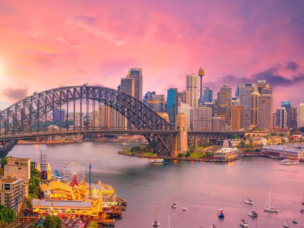 Cityscape with Sydney Harbour Bridge and high rise buildings of Sydney viewed across a bay where many small boats are moored during sunset