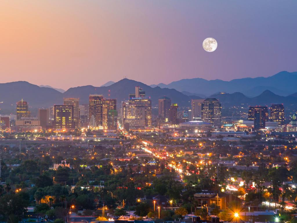 Cityscape during sunset with mountains in the background and full moon in the sky