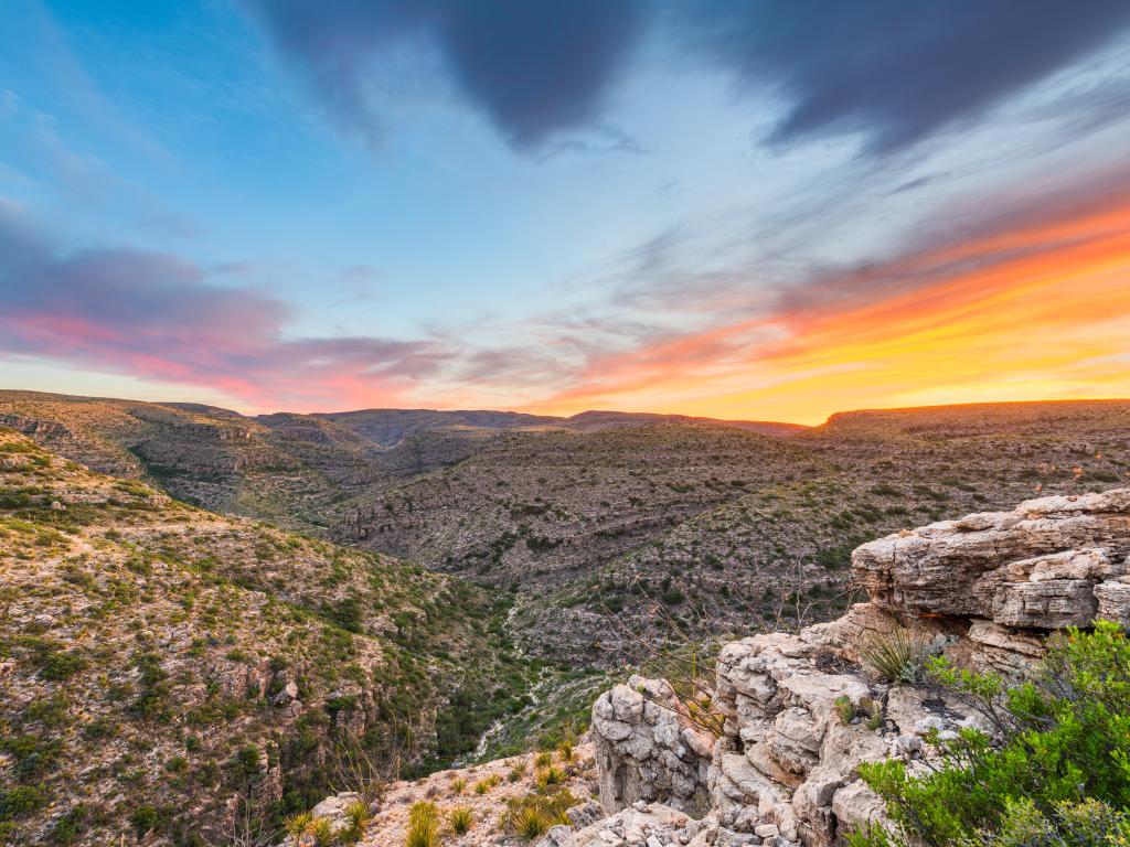 Carlsbad Caverns National Park, New Mexico looking to the valley below with mountain terrain above a sunset sky.