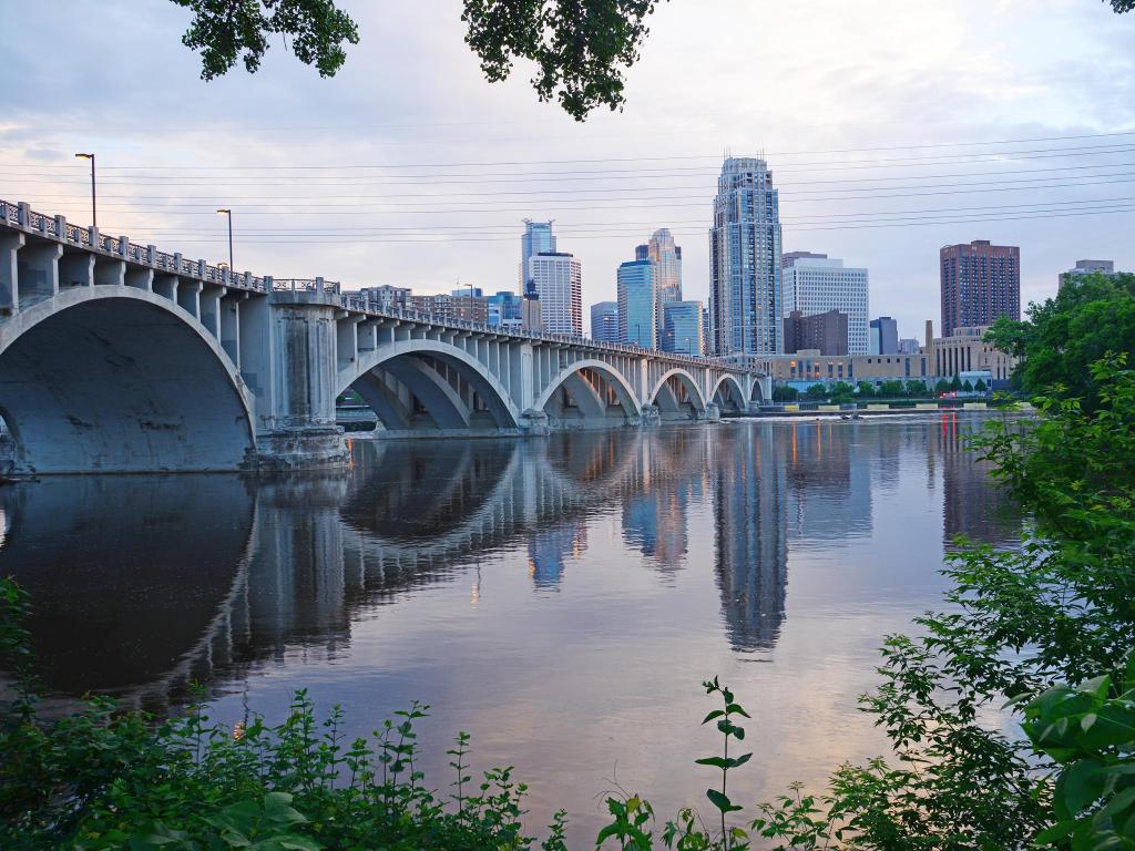 Minneapolis, Minnesota, USA with a city view of Minneapolis in an evening with a bridge crossing the river in the foreground.