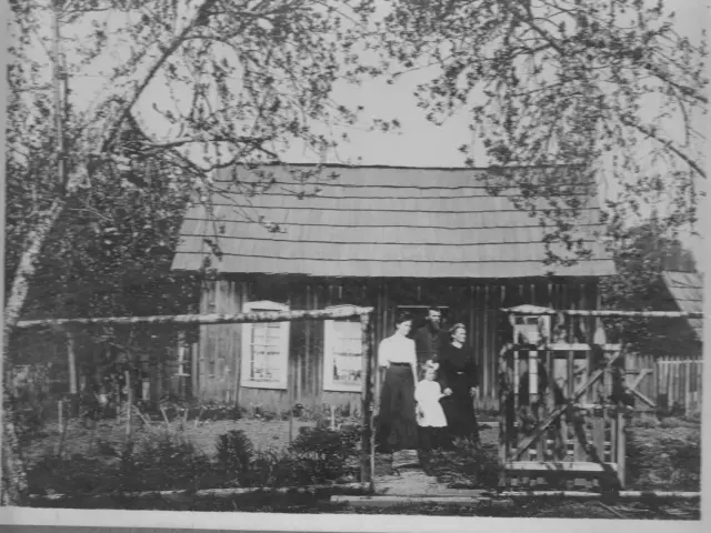 Black and white photo of early settlers, standing in front of their house