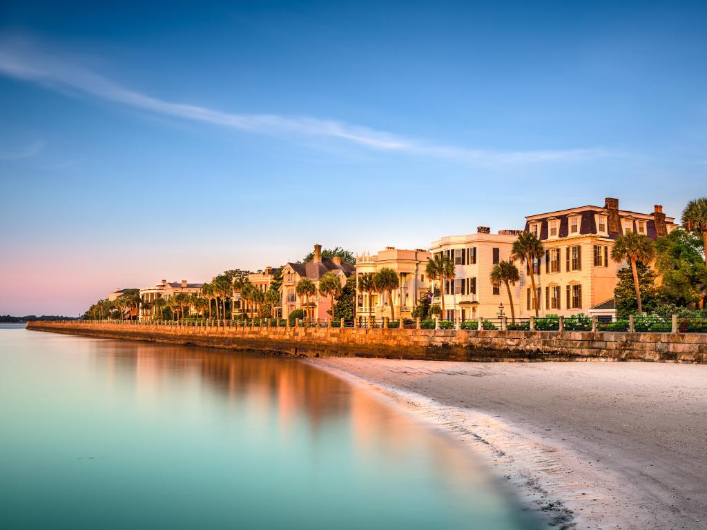 Historic white buildings right on the waterfront with palm trees in a row and a small section of beach