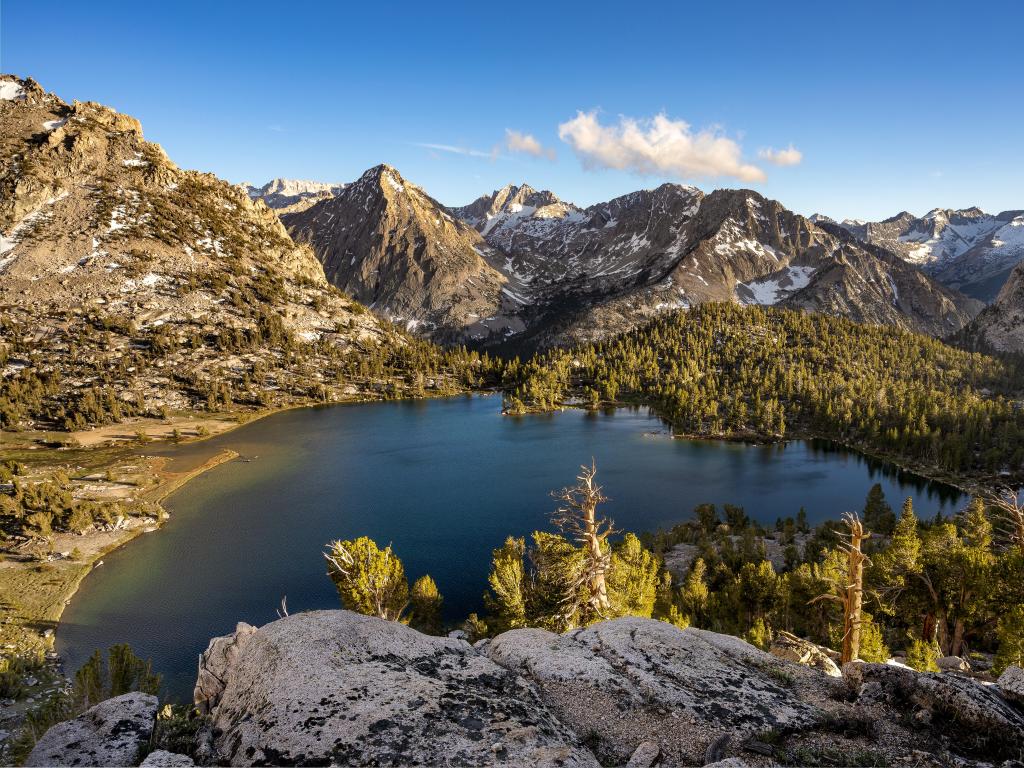 Kings Canyon National Park, California with Alpine Lake in the foreground and mountains with sprinklings of snow in the background below a blue sky.
